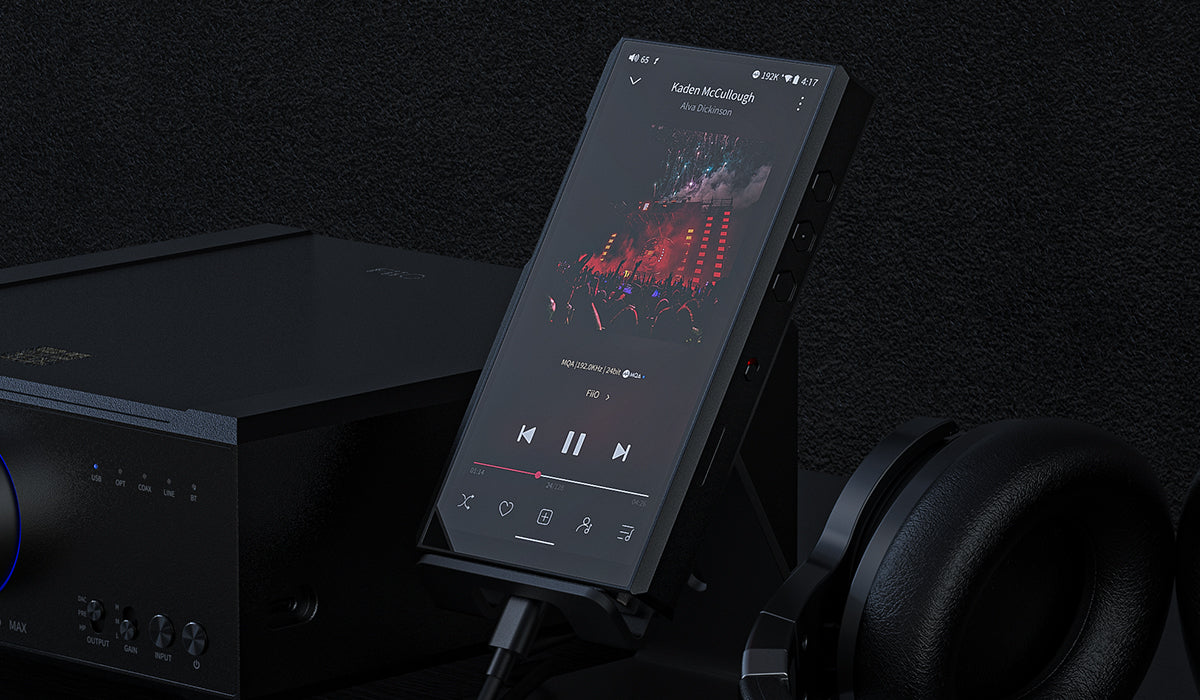 fiio m11 plus digital audio player in the center of the picture. black background with black amplifier in the left side of the player and over ear black headphone in the right side of the player.