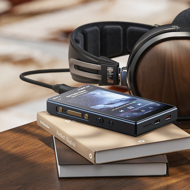 נגן אודיו דיגיטלי fiio m21 dap מונח על צמד ספרים הנמצאים על מדף עץ ולצידם אוזניות קשת fiio ft1 המחוברים לנגן בכבל שחור